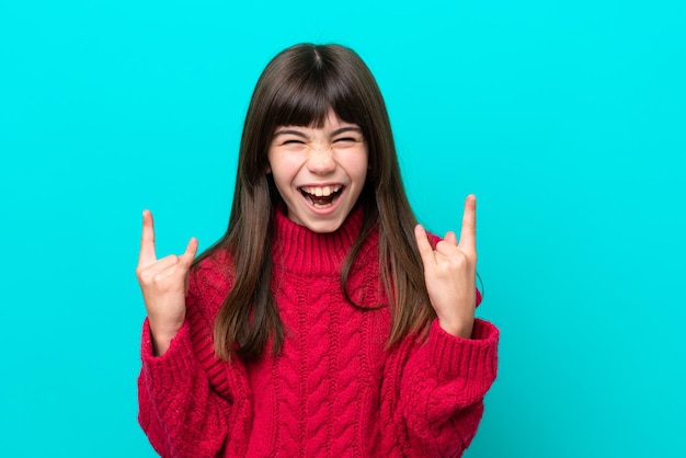 Niña caucásica aislada sobre fondo azul haciendo gesto de cuerno