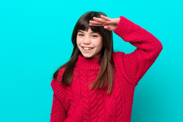 Niña caucásica aislada sobre fondo azul saludando con la mano con expresión feliz