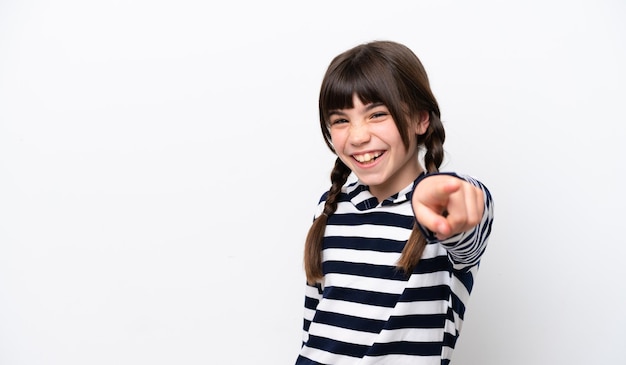 Niña caucásica aislada sobre fondo blanco apuntando al frente con expresión feliz