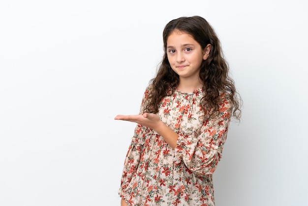 Niña caucásica aislada sobre fondo blanco presentando una idea mientras mira sonriendo hacia