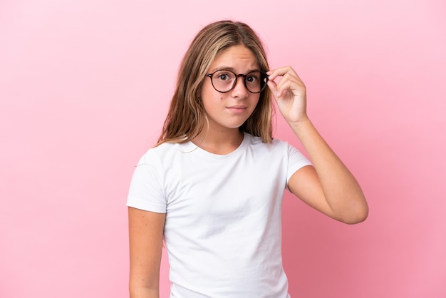 Niña caucásica aislada sobre fondo rosa Con gafas y expresión frustrada