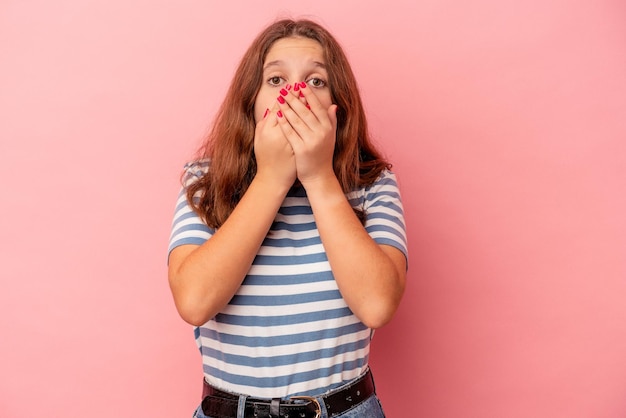 Niña caucásica aislada sobre fondo rosa sorprendido cubriendo la boca con las manos.