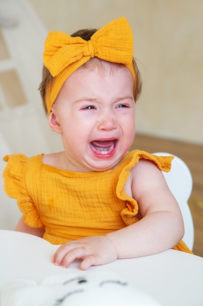 Una niña caucásica de un año con ropa amarilla está molesta y llorando, foto de estudio de un niño de un año