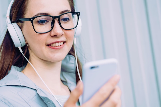 Niña caucásica en auriculares sonríe y escucha música mientras mira en un teléfono inteligente