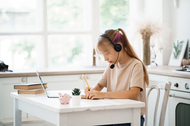 Niña caucásica en auriculares tiene videollamada a clase distante con el maestro en casa