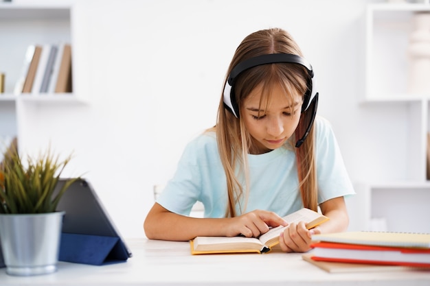 Niña caucásica en auriculares tiene videollamada a clase distante con el maestro en casa