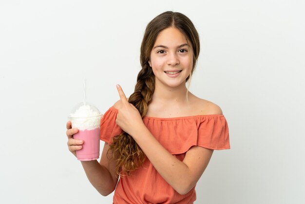 Niña caucásica con batido de fresa aislado sobre fondo blanco apuntando hacia atrás