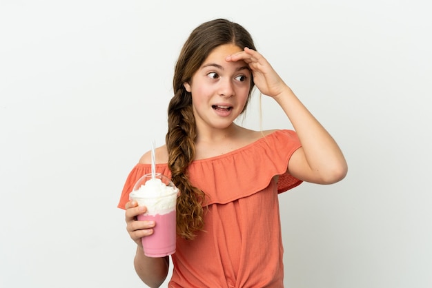 Niña caucásica con batido de fresa aislado sobre fondo blanco haciendo gesto de sorpresa mientras mira hacia el lado