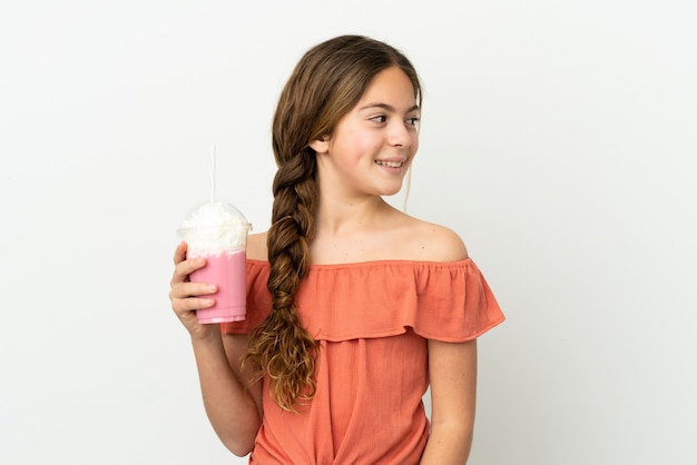 Niña caucásica con batido de fresa aislado sobre fondo blanco mirando de lado