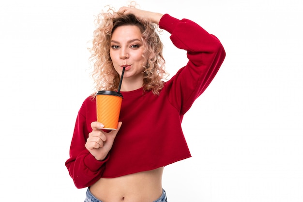 Niña caucásica con cabello rubio rizado bebe café y sonrisas, retrato aislado