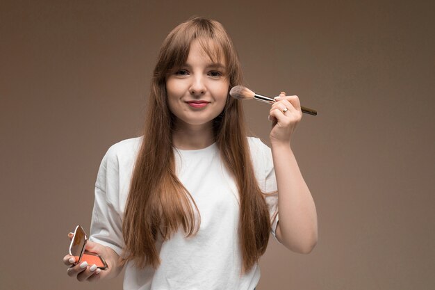 Niña caucásica en una camiseta blanca con pincel de maquillaje en una pared oscura