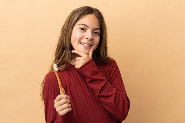 Niña caucásica cepillarse los dientes aislado sobre fondo beige feliz y sonriente