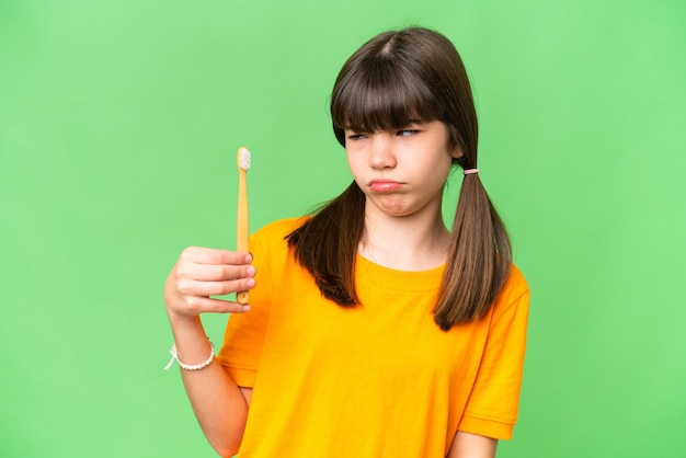 Niña caucásica cepillarse los dientes sobre un fondo aislado con expresión triste