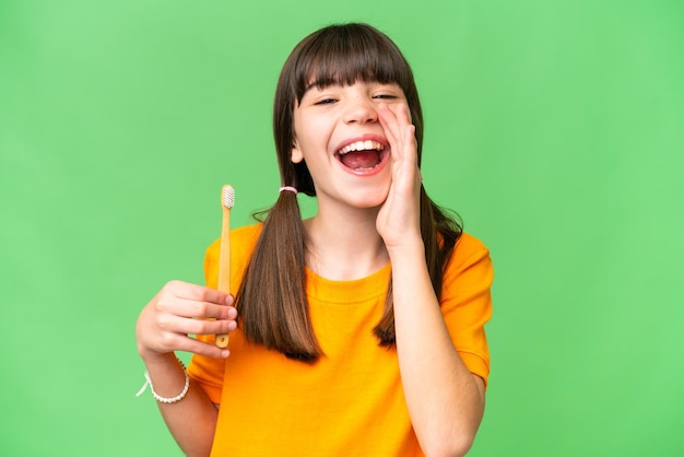 Niña caucásica cepillarse los dientes sobre un fondo aislado gritando con la boca abierta