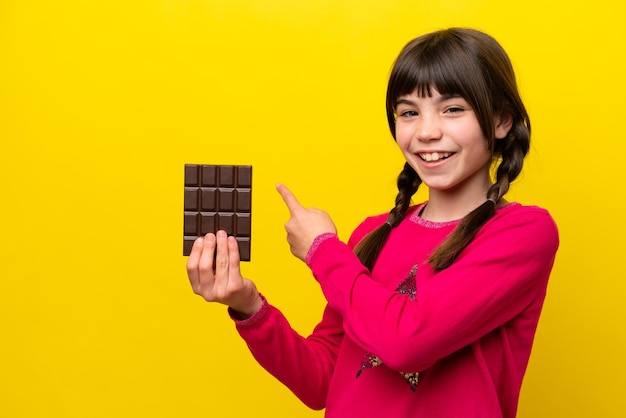 Niña caucásica con chocolat aislado sobre fondo amarillo apuntando hacia atrás