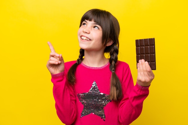 Niña caucásica con chocolat aislado sobre fondo amarillo apuntando a una gran idea