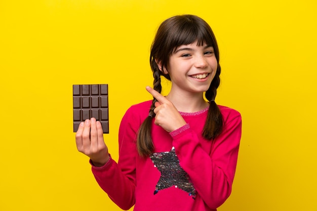 Niña caucásica con chocolat aislado sobre fondo amarillo apuntando hacia un lado para presentar un producto