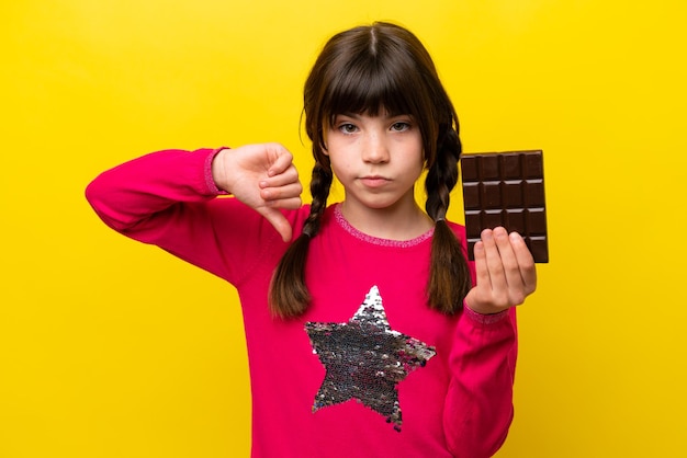 Foto niña caucásica con chocolat aislado sobre fondo amarillo mostrando el pulgar hacia abajo con expresión negativa