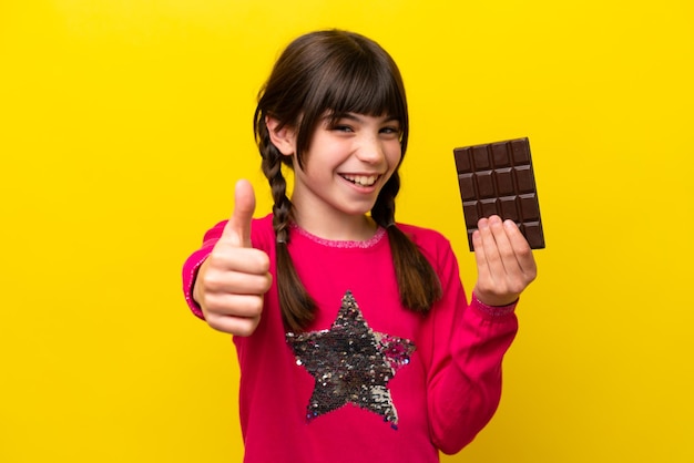 Foto niña caucásica con chocolat aislado sobre fondo amarillo con los pulgares hacia arriba porque algo bueno ha sucedido