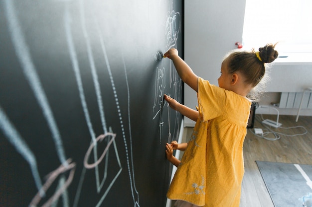 Niña caucásica dibuja en la pared con pizarra