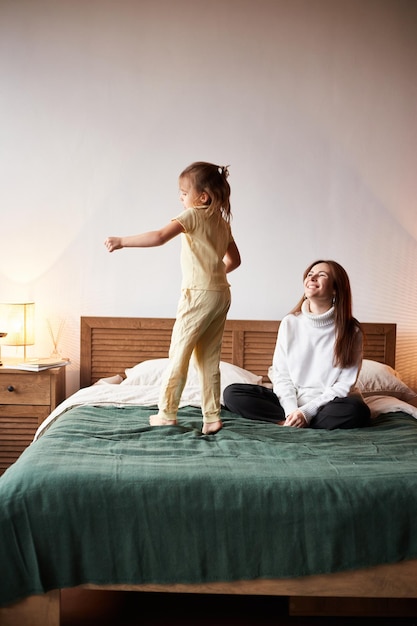 Niña caucásica diviértete con la madre Saltando en la cama la mañana de Navidad Concepto de Navidad familiar feliz