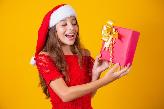 Niña caucásica emocionada con la boca abierta sosteniendo un regalo de Navidad.