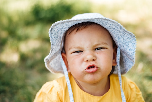 Niña caucásica hace una mueca a la cámara con sombrero y vestido amarillo