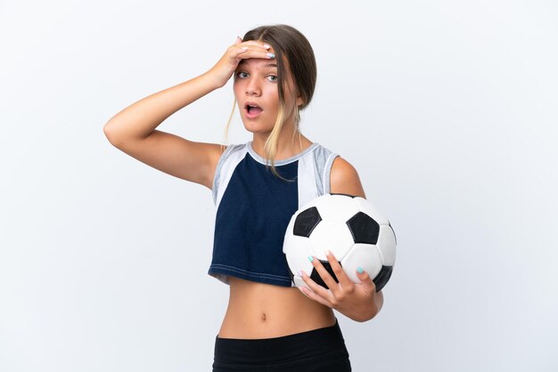 Foto niña caucásica jugando al fútbol aislado sobre fondo blanco haciendo gesto de sorpresa mientras mira hacia el lado