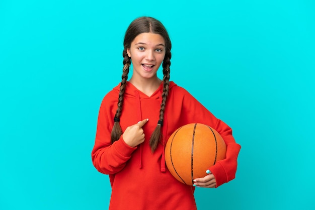 Niña caucásica jugando baloncesto aislada de fondo azul con expresión facial sorpresa