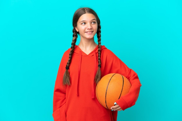 Niña caucásica jugando baloncesto aislada de fondo azul pensando en una idea mientras mira hacia arriba