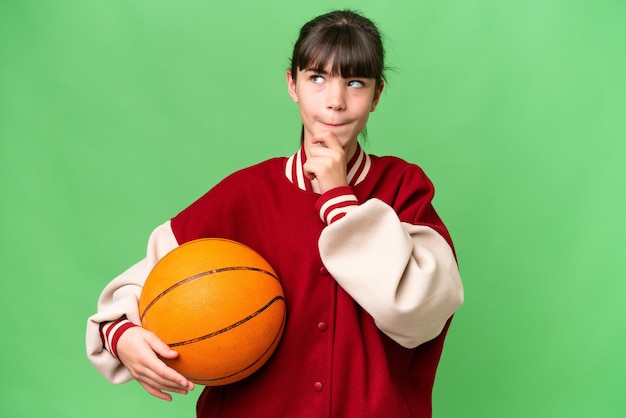 Niña caucásica jugando baloncesto sobre un fondo aislado que tiene dudas y pensamiento