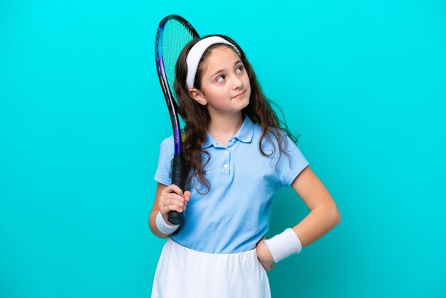 Niña caucásica jugando tenis aislada de fondo azul mirando hacia arriba mientras sonríe