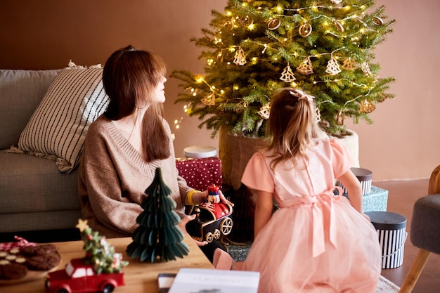 Niña caucásica con madre desempacando cajas de regalo en casa árbol de Navidad Concepto de Navidad familiar feliz