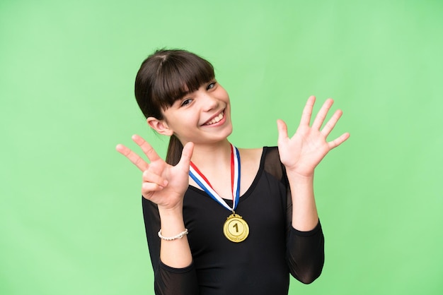 Foto niña caucásica con medallas sobre antecedentes aislados contando ocho con los dedos