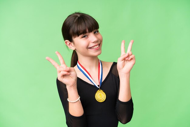 Niña caucásica con medallas sobre un fondo aislado que muestra el signo de la victoria con ambas manos