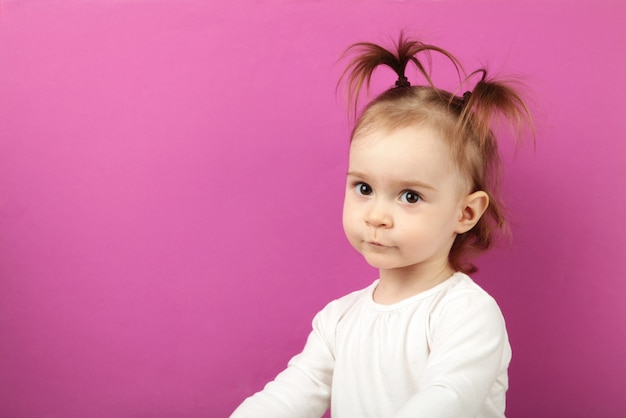 Niña caucásica mirando con adorable sonrisa, posando en rosa. Concepto de infancia feliz con espacio de copia