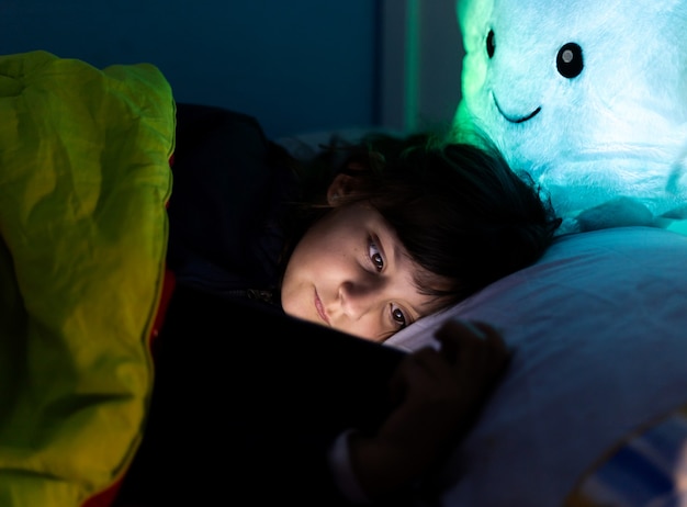 Niña caucásica, mirando la tableta, en la cama antes de acostarse