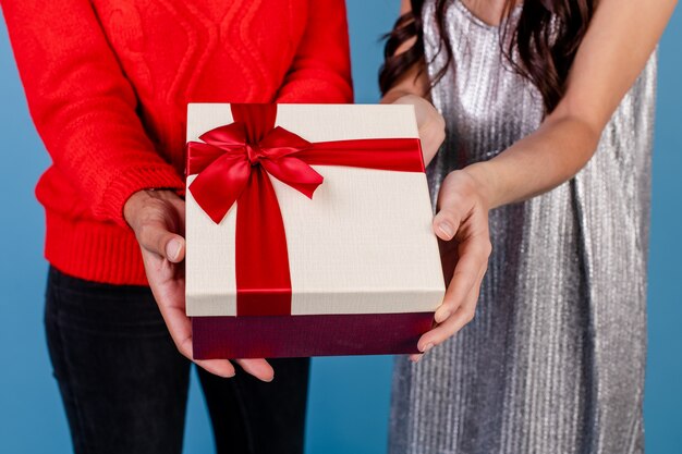 Niña caucásica y mujer negra con caja de regalo aislada sobre azul