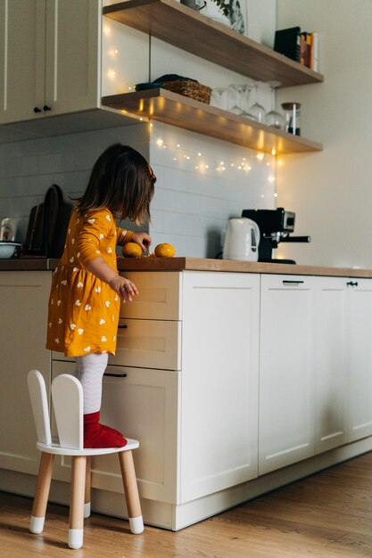 Niña caucásica pelando mandarinas en la cocina. Dieta infantil saludable. Impulso inmunológico con