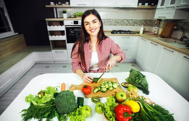 Niña caucásica de pelo largo disfrutando de una saludable ensalada mixta en una mesa llena de frutas y verduras en una cocina grande y luminosa