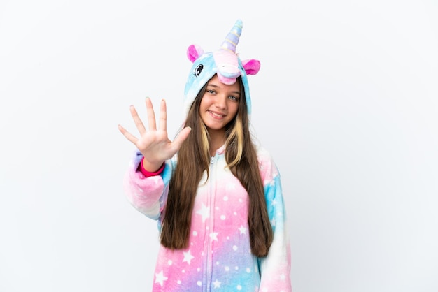 Niña caucásica con pijama de unicornio aislada de fondo blanco contando cinco con los dedos