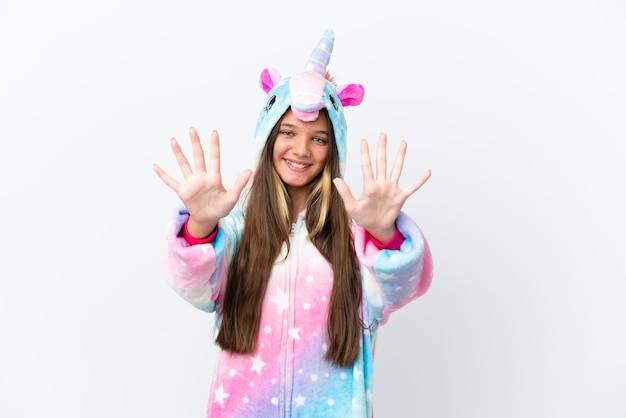 Niña caucásica con pijama de unicornio aislada de fondo blanco contando diez con los dedos