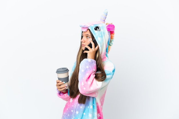 Niña caucásica con pijama de unicornio aislada de fondo blanco sosteniendo café para llevar y un móvil