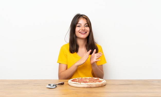 Niña caucásica con una pizza aplaudiendo