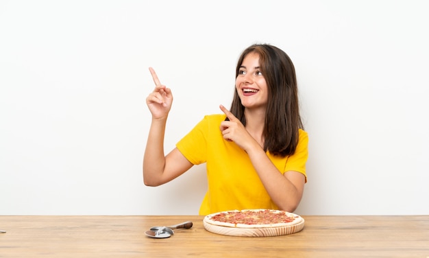 Foto niña caucásica con una pizza apuntando con el dedo índice una gran idea