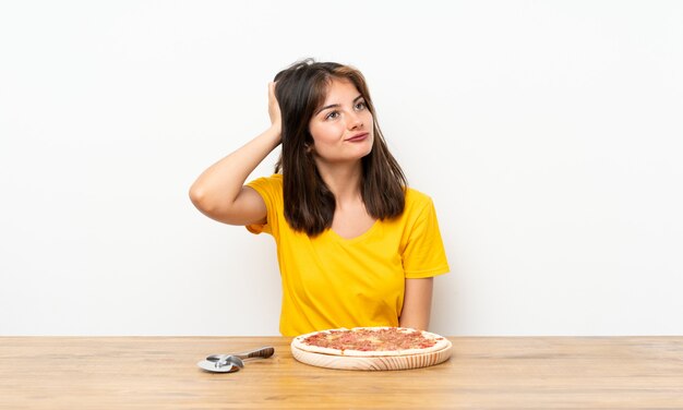 Niña caucásica con una pizza que tiene dudas y con expresión de la cara confusa