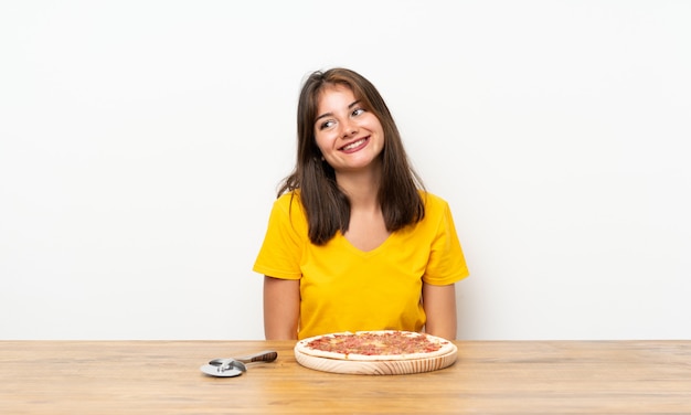 Niña caucásica con una pizza riendo y mirando hacia arriba