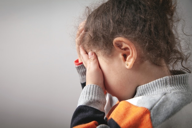 Niña caucásica que cubre su rostro con las manos.