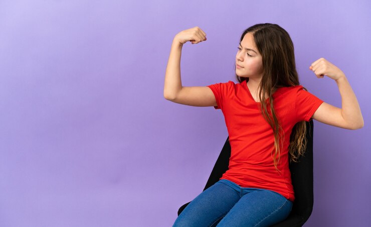 Foto niña caucásica sentada en una silla aislada sobre fondo púrpura haciendo gesto fuerte