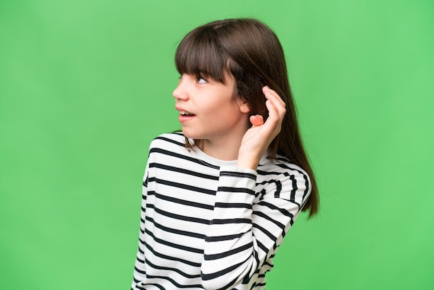 Niña caucásica sobre un fondo aislado escuchando algo poniendo la mano en la oreja